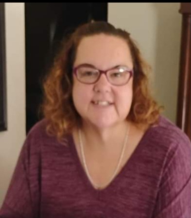 A woman with curly hair and glasses faces the camera