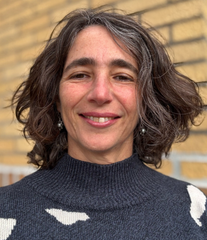 A woman faces the camera in front of a brick wall