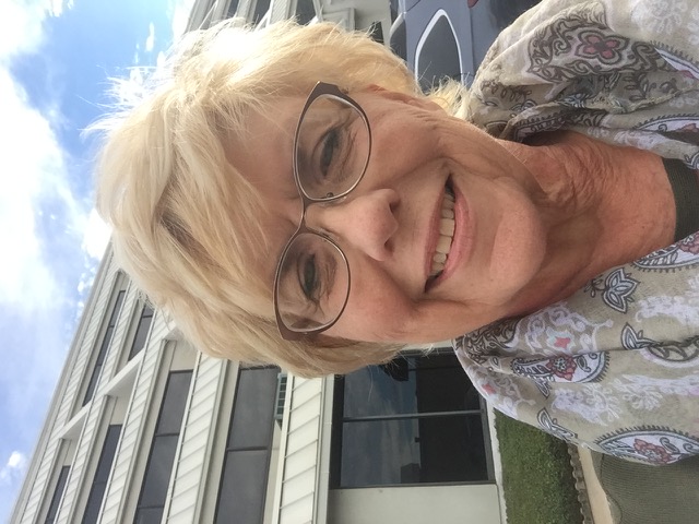 A woman wears glasses and a patterned scarf outdoors near a building