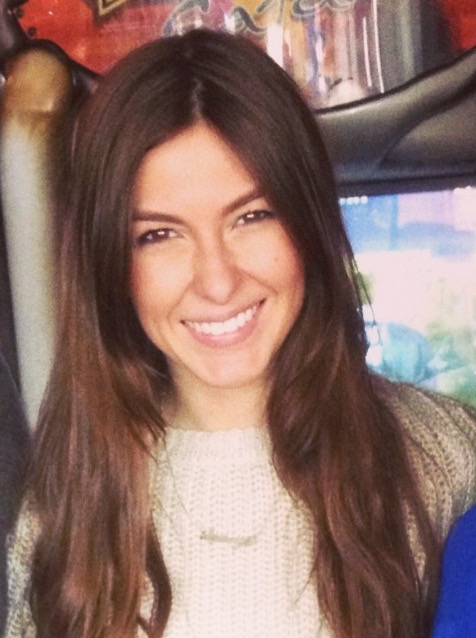 A woman faces the camera with long hair and a wide smile