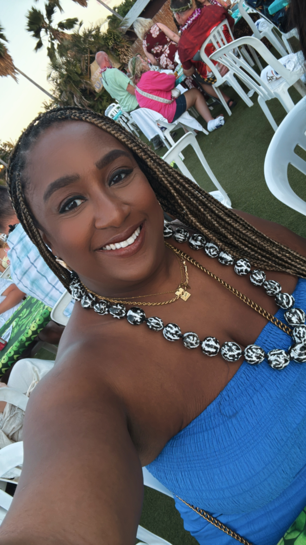 A woman takes a selfie at an outdoor gathering with people seated at tables behind her