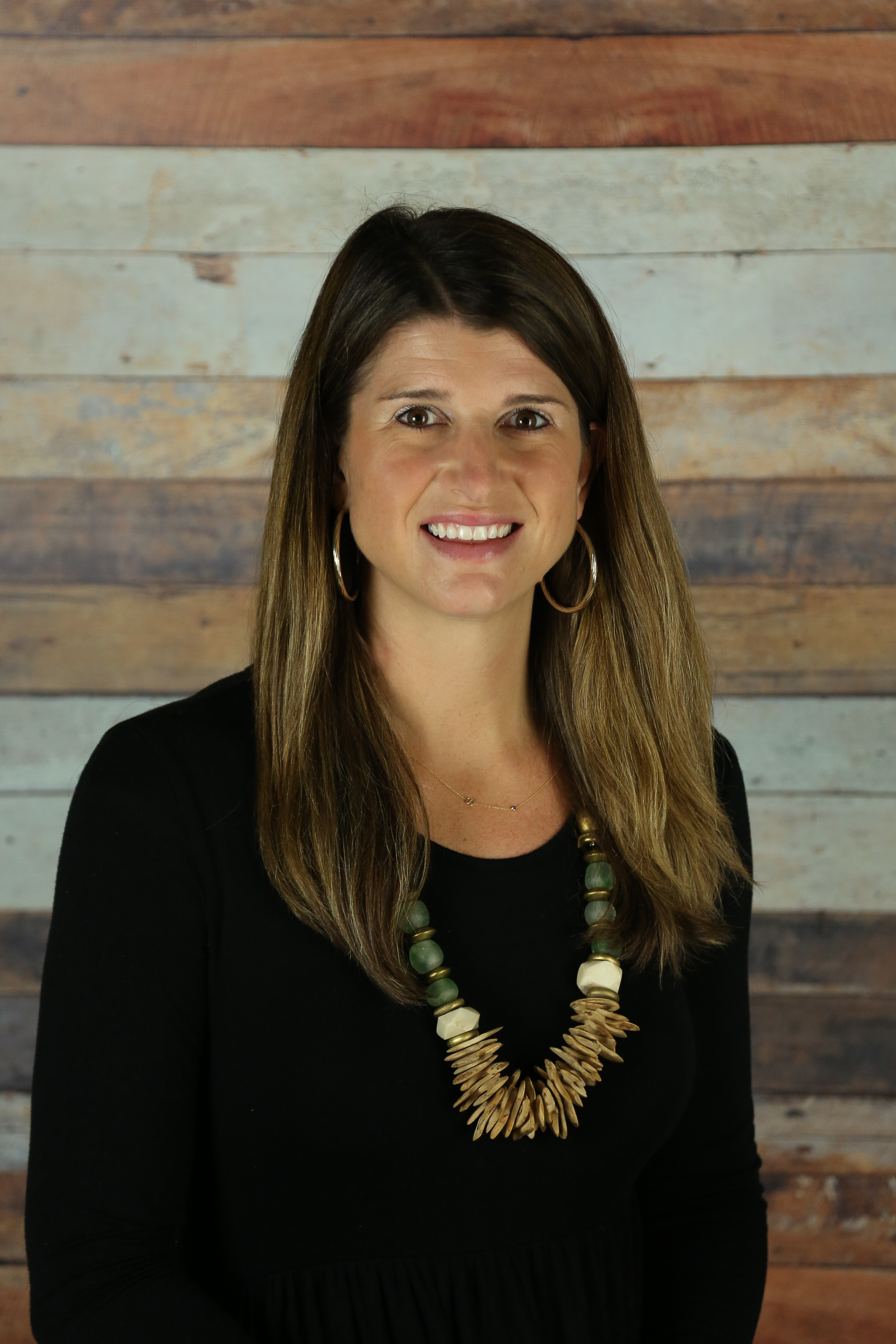 A woman poses in front of a rustic wood plank wall