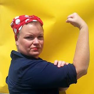 A woman wears a red polka-dot bandana and flexes one arm in a classic pose