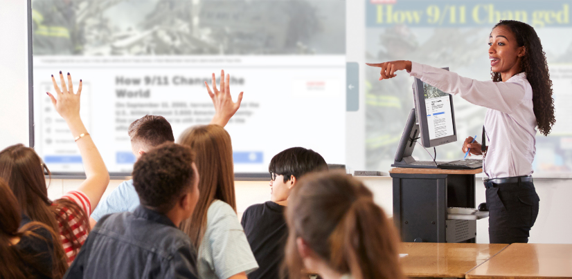 A woman points to a projected screen titled How 9/11 Changed the World as students raise their hands