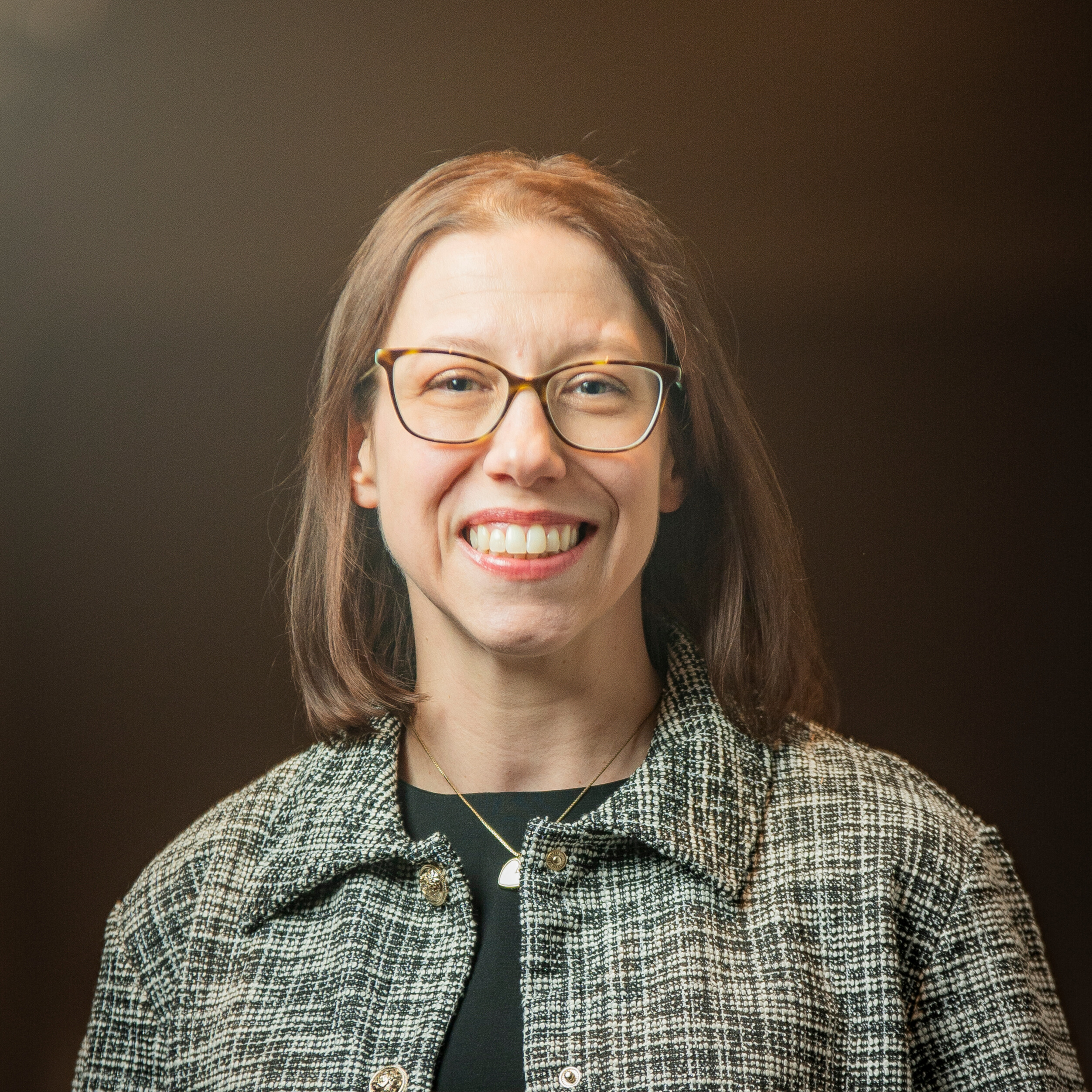 A woman with glasses faces the camera against a dark background