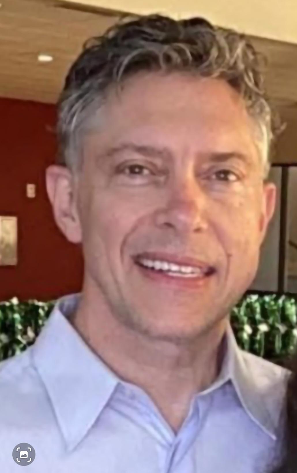 A man with gray curly hair faces the camera indoors